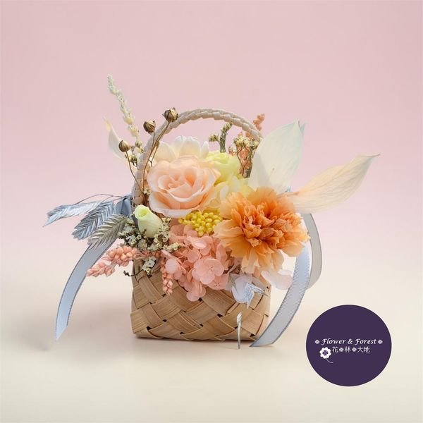 This hand‑woven arrangement features orange carnation, peach and cream roses, cheerful yellow accents, soft hydrangeas, and elegant sola flower — all preserved to retain their beauty for years. A silver ribbon and golden touches complete the look, making it both sophisticated and heart‑warming.